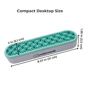 May include: A rectangular organizer with a light gray base and a mint green silicone insert featuring a repeating geometric flower pattern. The text "colornook" and a small dog logo are printed on the side. Dimensions are 8.27 inches by 2 inches by 1.26 inches.