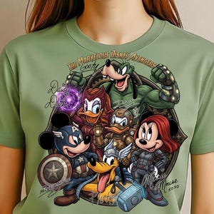 May include: Sage green t-shirt featuring a graphic of Disney characters as Avengers. The design includes Mickey Mouse as Captain America, Minnie Mouse as Black Widow, and Goofy. Text reads "The Marvelous Disney Avengers".