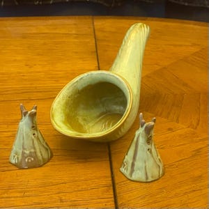 May include: A ceramic salt and pepper set featuring a horn-shaped salt cellar and two teepee-shaped shakers. The set is in shades of green and brown, with a glossy finish. The salt cellar is approximately 6 inches long.