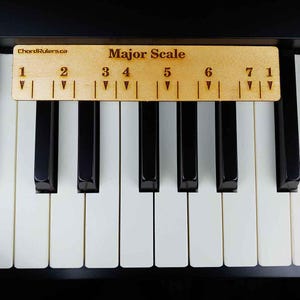 Könnte beinhalten: Ein helles Holz-Führungswerkzeug mit der Aufschrift Major Scale, den Zahlen eins bis sieben und nach unten zeigenden Dreiecken, das horizontal auf den schwarzen und weißen Tasten eines Klaviers liegt. Der Text ChordRulers.ca ist sichtbar.