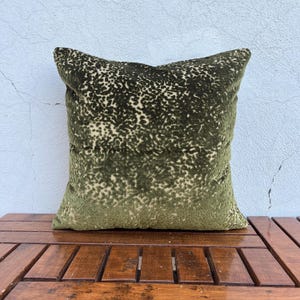 May include: A square throw cushion featuring a deep olive green velvet fabric with a textured, raised animal-inspired pattern. The surface displays a dense, mottled design in varying shades of dark green and lighter, muted olive tones throughout.