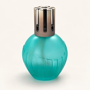 May include: A round, teal-colored glass fragrance lamp with a frosted finish and vertical ribbed detailing at the base. The top features a metallic, bronze-toned vented cap with a circular cutout design, securely fitted onto the glass vessel.