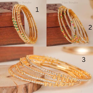 May include: Three sets of gold-toned bangles labeled 1, 2, and 3. Set 1 features green and pink stones. Set 2 features green and pink stones in a different pattern. Set 3 consists of gold bangles encrusted with clear white stones throughout.
