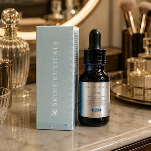 May include: A skincare product set featuring a dark blue glass bottle with a dropper and a matching box. The bottle and box display the "SkinCeuticals" brand name and product information. The bottle contains 15 ml / 0.5 fl oz of serum.