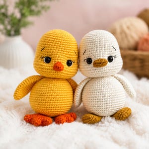 Può includere: Due peluche amigurumi a forma di piccoli uccelli. Uno è giallo brillante con becco e zampe arancioni, mentre l'altro è bianco sporco con becco e zampe marrone chiaro. Entrambi hanno occhi neri rotondi con ciglia ricamate e finitura in filato.