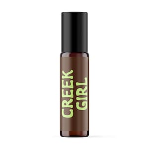 May include: A cylindrical amber glass roller bottle with a black cap. The label on the front of the bottle features the text CREEK GIRL printed in a light lime green colour, oriented vertically along the length of the bottle body.