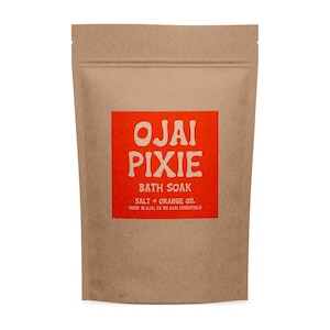 Könnte beinhalten: Ein brauner Papiersack mit Ojai Pixie Badesalz. Der Beutel hat ein rotes quadratisches Etikett mit weißem Text: "OJAI PIXIE BATH SOAK SALT + ORANGE OIL". Der Beutel ist oben versiegelt.