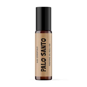May include: A cylindrical amber glass perfume oil roll-on bottle with a black cap. The label is tan paper with black text that reads Ojai Essentials, Palo Santo, and Perfume Oil Roll-on. The bottle is upright and features a simple, clean design.
