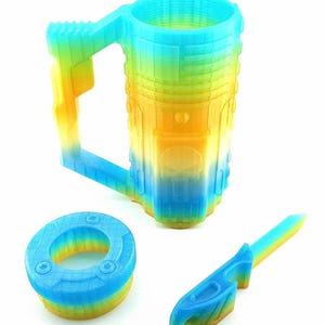 May include: A 3D-printed mug, a small circular object, and a knife-like object. All items are in a gradient of blue, yellow, and green. The mug has a handle and a cylindrical shape. The other objects have a similar color scheme.