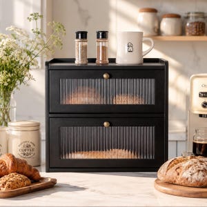 May include: A black two-tier storage cabinet with fluted glass doors and small gold knobs. The unit features two horizontal drawers with ribbed transparent panels, providing a view of the contents inside. The frame is solid black wood.