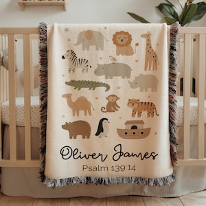 May include: Cream-colored baby blanket with a colorful animal print, including a zebra, lion, and giraffe. The blanket has a fringed edge and the name "Oliver James" and the text "Psalm 139:14" are printed on the blanket.