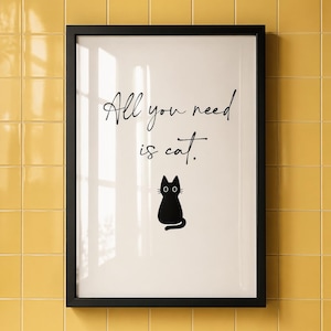 Può includere: Una stampa incorniciata con la scritta "All you need is cat" in corsivo nero, sopra una silhouette di gatto nero. La cornice nera contrasta con lo sfondo bianco. La stampa è montata su una parete piastrellata gialla.