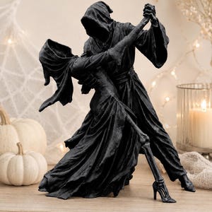 May include: A matte black sculpture depicting two hooded figures in a dance pose. One figure wears a long flowing robe, while the other figure wears a long dress and has a visible skeletal leg extending from the hem, ending in a high-heeled shoe.