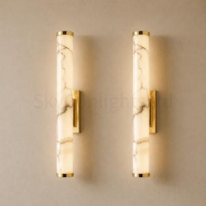 Puede incluir: Dos apliques de pared verticales con un diseño similar al mármol y detalles dorados. Los apliques tienen forma rectangular y están montados en una pared de color neutro. El texto "Skylight" es visible.