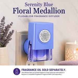 May include: A Serenity Blue Floral Medallion Plugables fragrance diffuser plugged into a wall outlet. The device features a light blue rectangular housing with a silver circular floral medallion and a clear purple glass fragrance oil container.