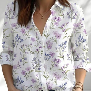 May include: A long-sleeved button-down shirt in white featuring a repeating pattern of light purple and blue wildflowers with green stems and leaves. The shirt has a classic collar, a front button placket, and long sleeves with cuffs.
