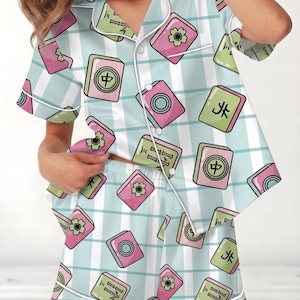 May include: Light blue pajama set with a repeating pattern of pink and green Mahjong tiles. The set includes a short-sleeved button-up shirt and matching shorts, both trimmed with white piping.