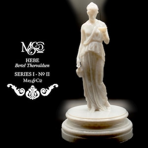 Puede incluir: Estatua de mármol blanco de una mujer sosteniendo una pequeña copa y una jarra. La estatua está sobre una base redonda escalonada. El texto a la izquierda dice "HEBE Bertel Thorvaldsen SERIES I - NO II May & Co."