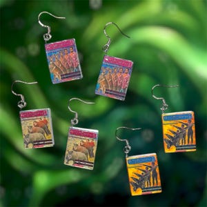 Puede incluir: Pendientes colgantes plateados con portadas de libros en miniatura con el título "Animorphs". Las portadas muestran ilustraciones de animales y personas. Los pendientes tienen cierre de gancho.