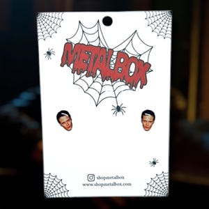 May include: White card with the text "METALBOX" in red dripping letters, spiderwebs, and small spiders. The card features two small images of a person's face. The shop's Instagram and website are listed.