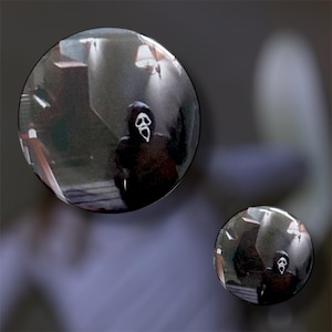 May include: Two round, reflective images of a figure in a black hooded robe and a white mask with a screaming face. The background is a dimly lit interior with stairs and a light fixture.