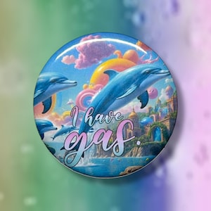 May include: A round button featuring a whimsical illustration of dolphins leaping in a blue ocean under a colorful sky. The button has the text "I have gas" in a cursive font.