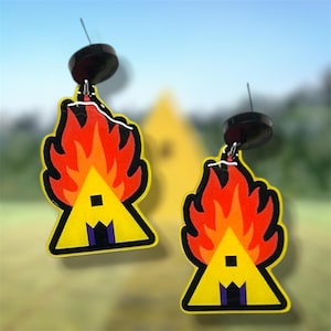 May include: A pair of dangle earrings featuring a yellow triangular house shape with a dark purple door and a small square window, topped with vibrant red and orange flames, attached to a black circular stud post with a silver metal connector.