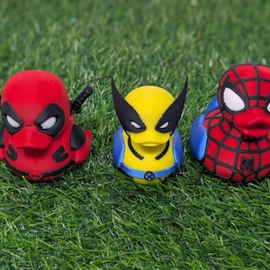 May include: Three rubber duck toys styled as Marvel comic book characters: Deadpool, Wolverine, and Spider-Man. The Deadpool duck is red with black accents and katanas. The Wolverine duck is yellow and blue with black mask. The Spider-Man duck is red and blue.