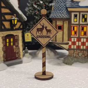 May include: A wooden sign with a brown background and a white diamond shape. The sign has a deer crossing graphic and the text "CROSSING". The sign is attached to a wooden post with a brown and white striped pole.