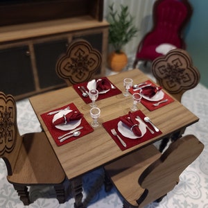 May include: A miniature wooden dining table set with four chairs, each with a carved snowflake design. The table is set with four place settings, each with a red napkin, a white plate, and silver cutlery. There are also four wine glasses on the table.