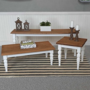 May include: Three wooden coffee tables with white painted legs. The largest table is in the background and the smallest table is in the foreground. The tables are on a striped rug.