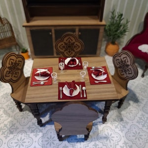 May include: A wooden dining table set with four chairs, red placemats, white plates, and silverware. The table is set for a formal dinner.