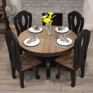 Peut inclure: Une table ronde en bois avec quatre chaises noires. La table est dress&eacute;e avec quatre couverts, chacun avec une assiette blanche, une serviette grise et un anneau de serviette argent&eacute;. Un vase avec des fleurs jaunes se trouve au centre de la table.