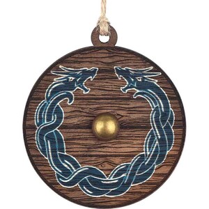 May include: A wooden ornament shaped like a shield with two blue dragons intertwined around the edge. The shield has a wood grain pattern and a gold metal center.