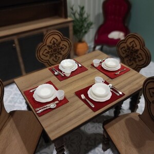 May include: A wooden dining table set with four chairs, each with a carved design. The table is set with four place settings, each with a white plate, a small bowl, and silverware. The place settings are on red placemats.