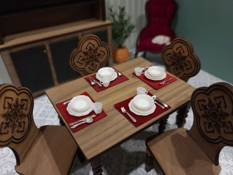 May include: A wooden dining table set with four chairs, each with a carved design. The table is set with four place settings, each with a white plate, a small bowl, and silverware. The place settings are on red placemats.