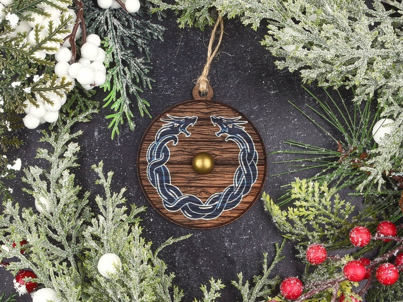 May include: A wooden Christmas ornament with a blue and black dragon design. The ornament is round and has a gold accent in the center.