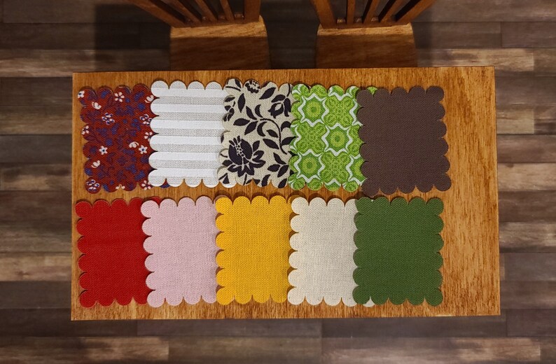 Puede incluir: Ocho cuadrados de tela festoneados en varios colores y patrones, incluyendo rojo, blanco, marr&oacute;n, verde, amarillo e impresiones florales. Los cuadrados est&aacute;n dispuestos en dos filas de cuatro sobre una superficie de madera.