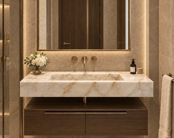 May include: A bathroom vanity featuring a rectangular white marble sink with brown veining, mounted above a dark wood floating cabinet with two drawers. A large rectangular mirror with gold trim hangs above the sink, flanked by warm LED lighting.