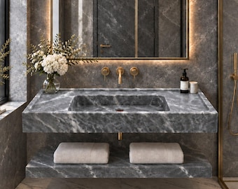 May include: A wall-mounted gray marble bathroom vanity featuring a rectangular integrated sink, a lower storage shelf holding two folded white towels, and gold-toned wall-mounted faucet fixtures, set against a matching gray marble wall.