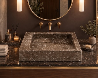 May include: A rectangular brown marble sink sits on a matching marble countertop with a dark wood vanity cabinet. Above the sink is a round mirror with a gold frame, flanked by two cylindrical pendant lights and gold wall-mounted faucets.