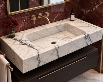 May include: A rectangular white marble sink with grey veining mounted on a dark wood floating vanity cabinet. The sink features a wall-mounted brass faucet with two handles and a matching towel bar holding a beige towel. A mirror hangs above.