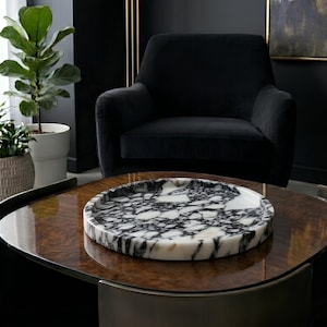 May include: A circular tray featuring a polished surface with a high-contrast black and white marble pattern. The tray has a low, raised rim and a smooth, glossy finish, showcasing natural veining throughout the stone material.