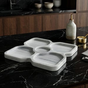 May include: A white marble serving tray featuring four square-shaped compartments and a small circular centre section. The tray has a smooth, polished finish with subtle grey veining throughout the stone surface, designed for organising food items.