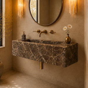 May include: A wall-mounted rectangular bathroom sink crafted from dark brown marble with prominent white veining. The sink features a brass faucet, two matching brass handles, a brass drain pipe, a soap dispenser, and a small vase with two white flowers.