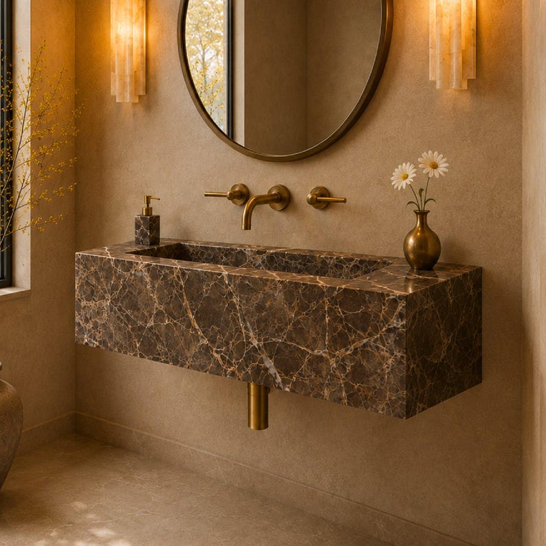 May include: A wall-mounted rectangular bathroom sink crafted from dark brown marble with prominent white veining. The sink features a brass faucet, two matching brass handles, a brass drain pipe, a soap dispenser, and a small vase with two white flowers.