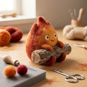 May include: A needle-felted orange and red flame-shaped creature with white eyes and a small smile, holding a textured gray log. The figure is surrounded by crafting supplies including a wooden needle tool, small yarn balls, and metal scissors.