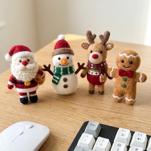 Puede incluir: Cuatro adornos navideños de fieltro: Papá Noel, un muñeco de nieve, un reno y un hombre de jengibre. Papá Noel tiene un traje rojo y barba blanca. El muñeco de nieve lleva una bufanda verde. El reno tiene cuernos. El hombre de jengibre tiene una pajarita roja.