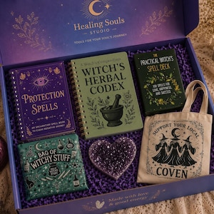May include: A gift box labeled Healing Souls Studio containing a purple Protection Spells book, a green Witch's Herbal Codex, a Practical Witch's Spell Deck, a Bag of Witchy Stuff, a heart-shaped amethyst crystal, and a beige tote bag with a Coven print.