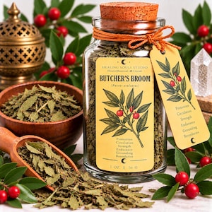 Puede incluir: Un frasco de vidrio transparente lleno de hojas secas de rusco, con un tapón de corcho y un cordel naranja. La etiqueta dice Butcher's Broom, 2 OZ, 56 G, y enumera propiedades como protección, circulación, fuerza, resistencia, conexión a tierra.